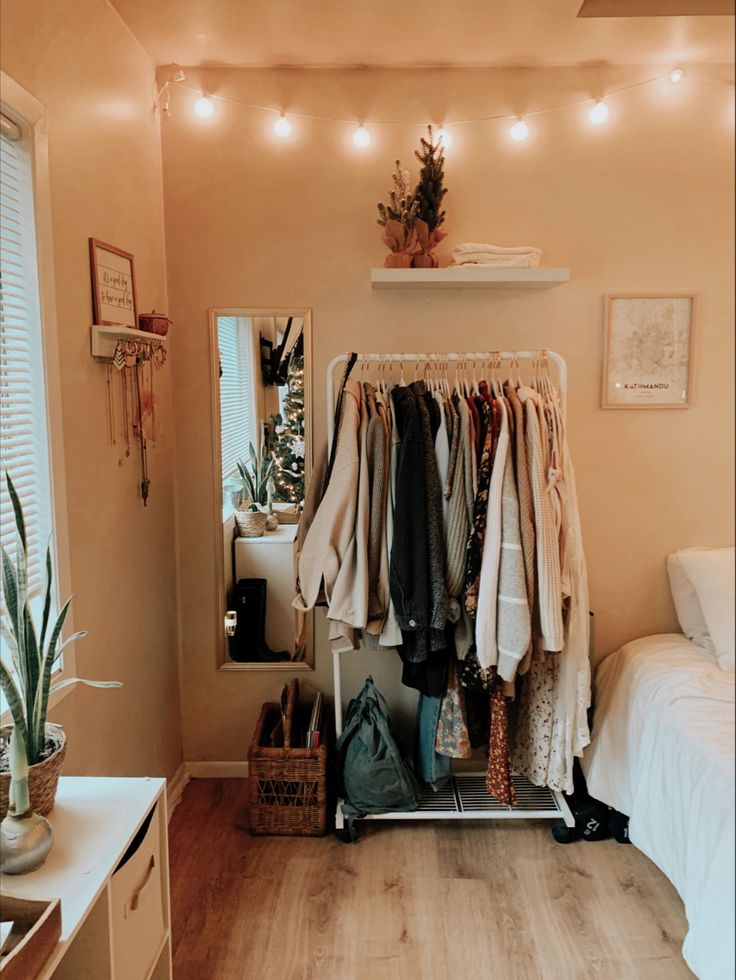 a small bedroom with clothes hanging on the rack and lights strung from the ceiling over the bed