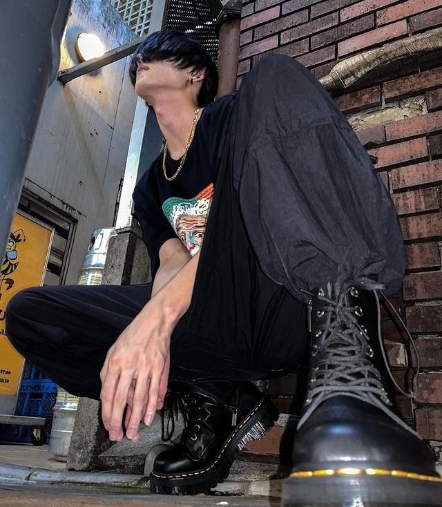 a woman sitting on the ground next to a brick wall with her hand in her shoe