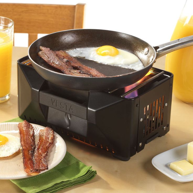 a frying pan with bacon and eggs on it sitting next to some glasses of orange juice