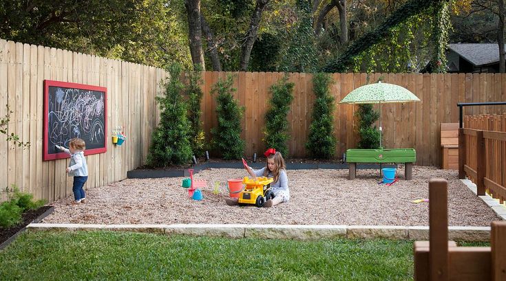 two children playing in a backyard sandbox