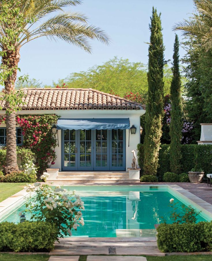 the pool is surrounded by greenery and palm trees in front of a white house