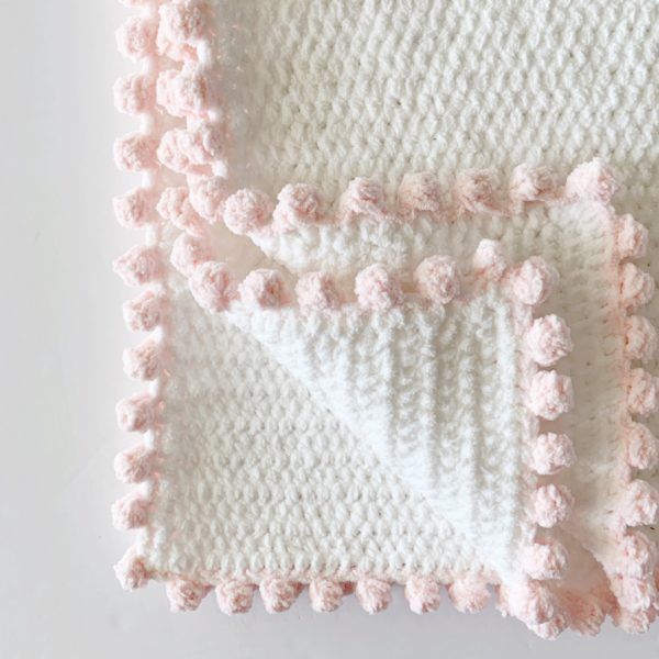 a crocheted blanket with pink pom - poms on the edges and bottom