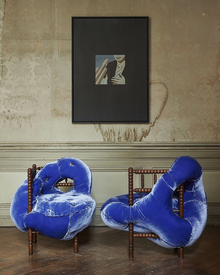 two blue chairs sitting next to each other in front of a painting on the wall