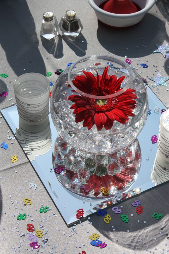 a glass vase with a red flower in it sitting on a table next to confetti