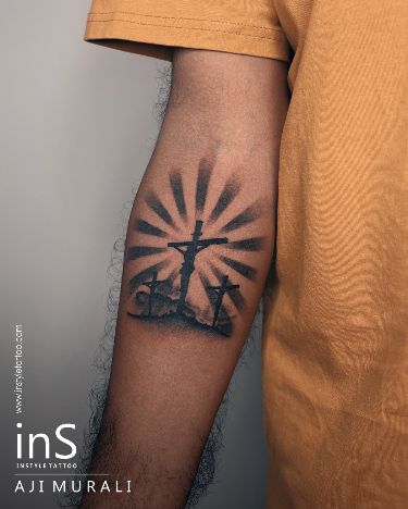 a man with a cross tattoo on his arm and the sun shining behind him in black ink