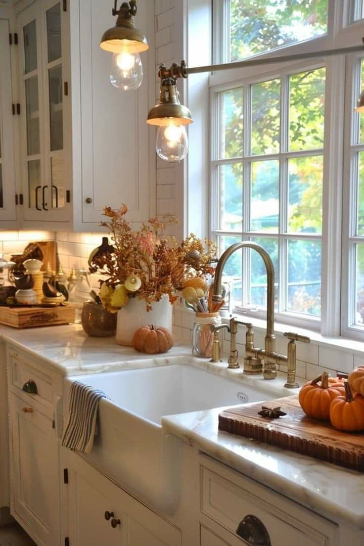 a kitchen with white cabinets and lots of pumpkins on the counter top in front of an open window