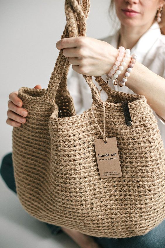 a woman holding a jute bag with a tag on the handle and string attached to it