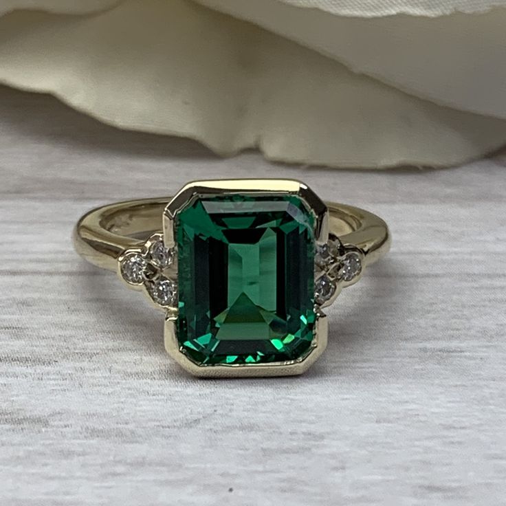 "The ring pictured is lab created emerald with moissanite accents #6974 -Approximate total carat weight: approx. 3.67ctw diamond equivalent -Center Stone Size: 10x8mm - approx. 3.55ct diamond equivalent -Center Stone Shape: emerald cut -Gem Type: lab created emerald -Stone Clarity: VS2 -Stone Color: green -Moh's Scale: 8.5 hardness -Side Stones Size: 6 round approx. 0.12ct. diamond equivalent -Gem Type: moissanite F VS2 -Metal Type and Purity: 14k yellow gold -Setting: half bezel design -Stock R Emerald Green Rings, Vintage Emerald Rings, Emerald Engagement Ring Set, Engagement Ring Emerald, Blue Sapphire Studs, Emerald Ring Vintage, May Birthstone Rings, Half Bezel, Bezel Set Ring