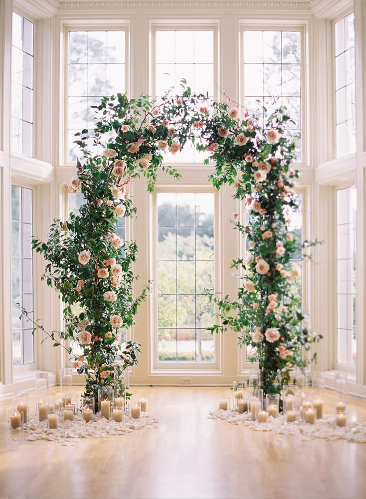 an arch with roses and candles in front of a window at a wedding ceremony or reception