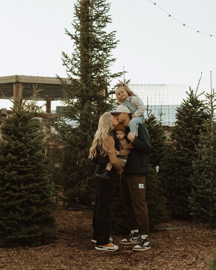 a man and woman are holding their child in front of christmas trees at the tree farm