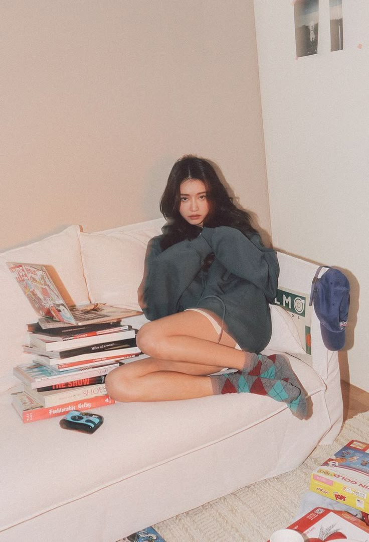 a woman sitting on top of a white couch next to stacks of books and magazines