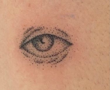 an eye tattoo on the back of a woman's shoulder, with dots all over it