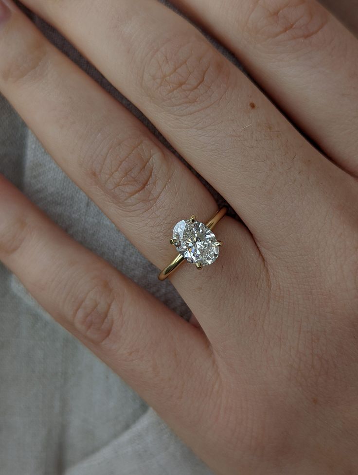 a woman's hand with a diamond ring on top of her finger and the other hand holding an engagement ring