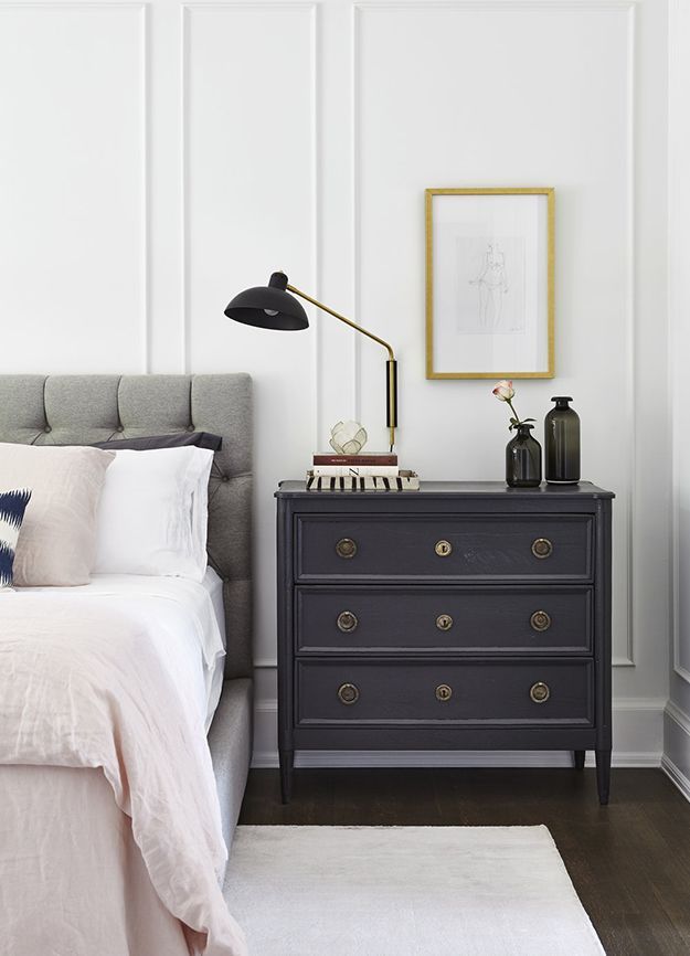 a bedroom with a bed, nightstand and lamp on it's side table in front of a white paneled wall