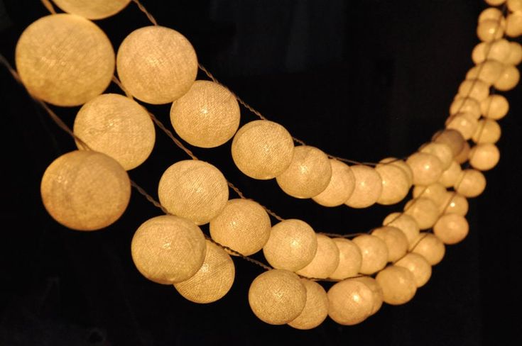 a string of wooden beads hanging from a black wall next to a lamp bulb light