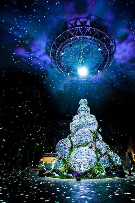 a large christmas tree is lit up at night with lights and snow flakes on the ground