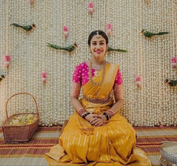 a woman sitting on the floor in a yellow sari with pink and white flowers behind her