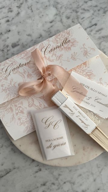 the wedding stationery is laid out on a marble plate with pink ribbon and matching tags