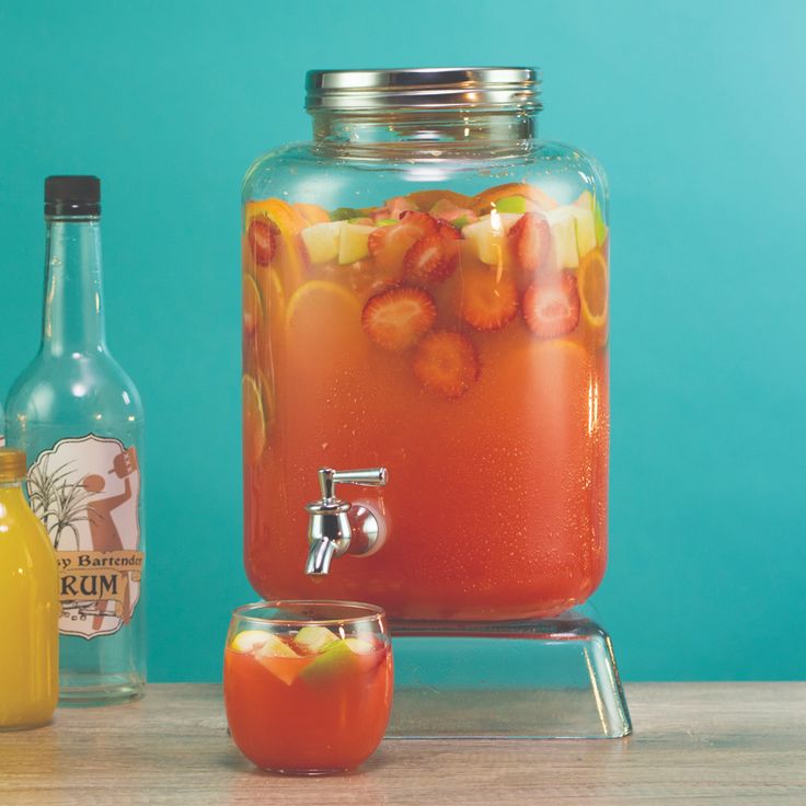 a beverage dispenser with fruit in it and two bottles next to it