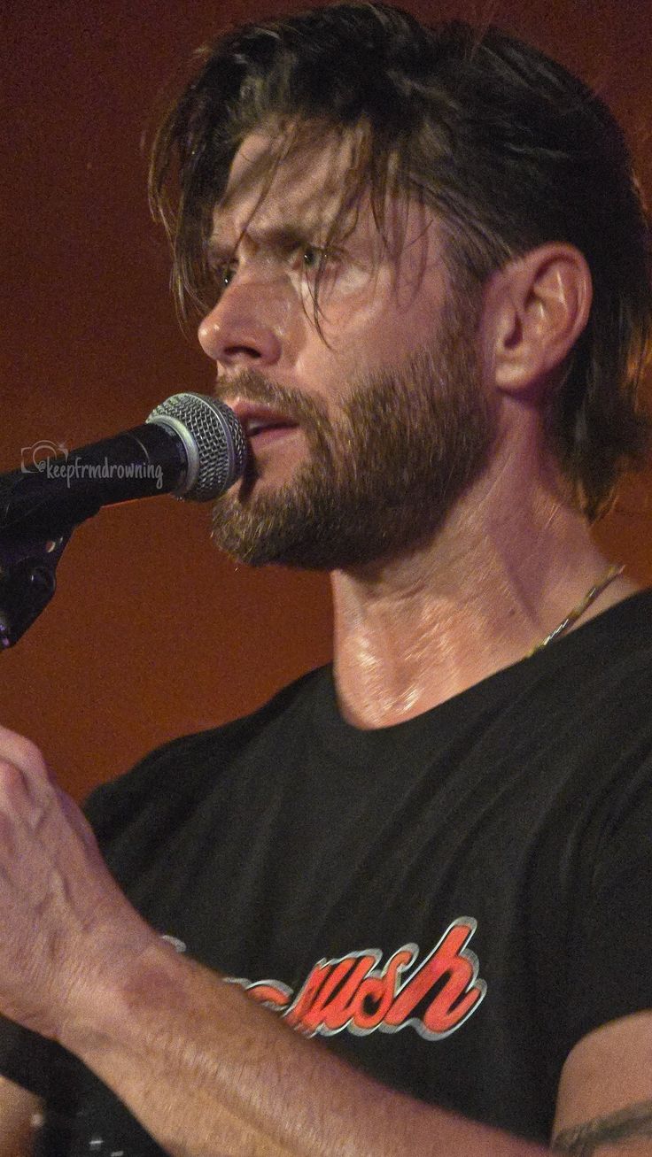 a man with long hair and beard holding a microphone in his hand while standing next to a microphone