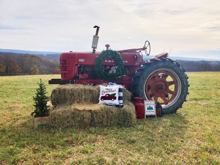 a red tractor parked on top of a grass field next to a pile of hay