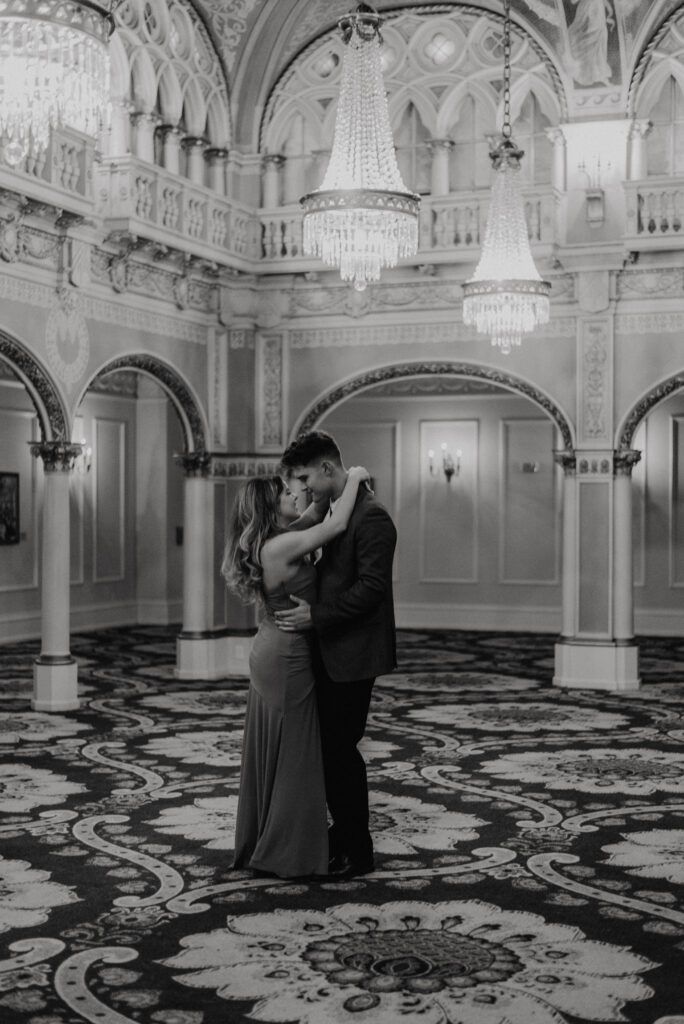 black and white photo of a couple embracing in an ornate ballroom with chandeliers