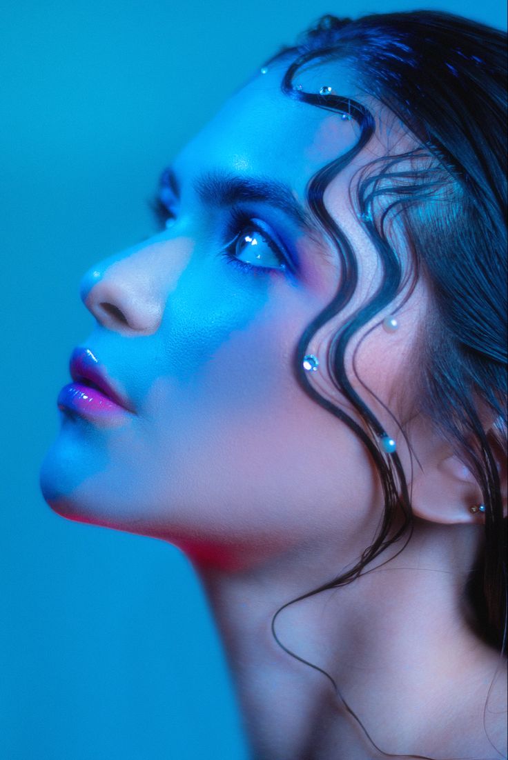 a woman with blue paint on her face and body is posing for a photo in front of a blue background