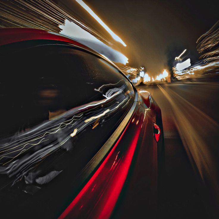 a red car driving down a street at night with motion blurs on the road