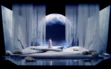 a woman standing in front of an ice cave with water and rocks on the ground