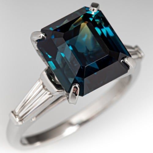 a blue diamond ring with baguets on the sides and an emerald stone in the center