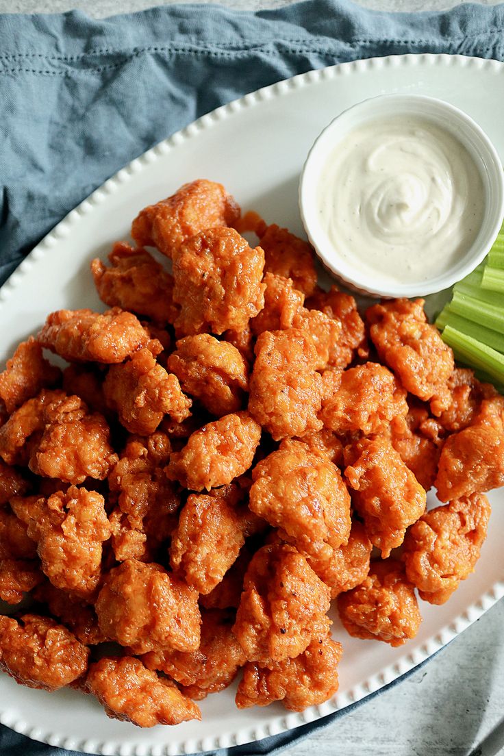 a white plate topped with fried chicken next to celery and ranch dressing on a blue cloth