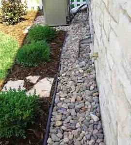 the side of a house with rocks and grass