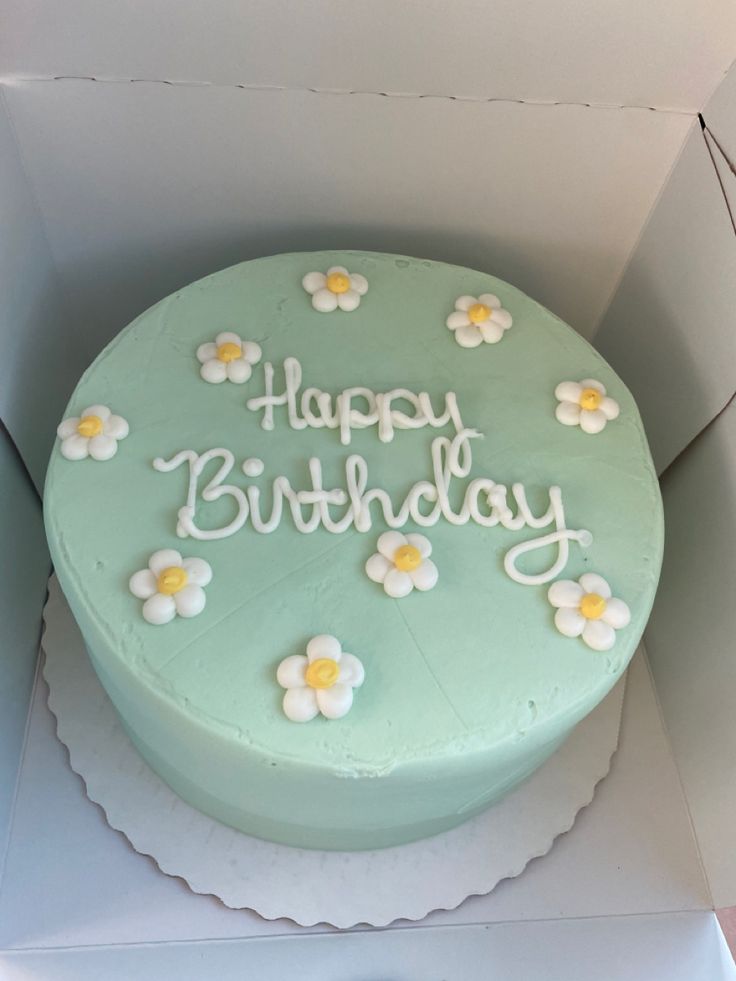 a green birthday cake with white and yellow flowers on the top is in a box