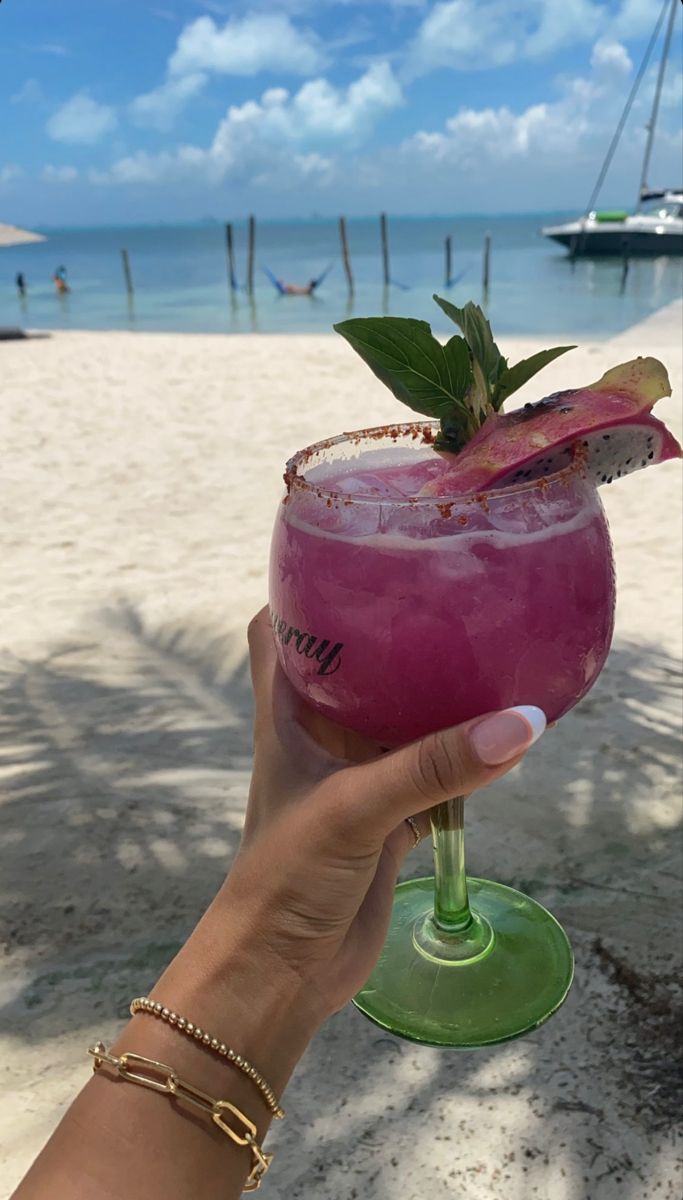 a person holding up a purple drink on the beach