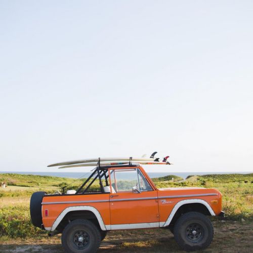 an orange and white truck with a surfboard on the roof parked in a field