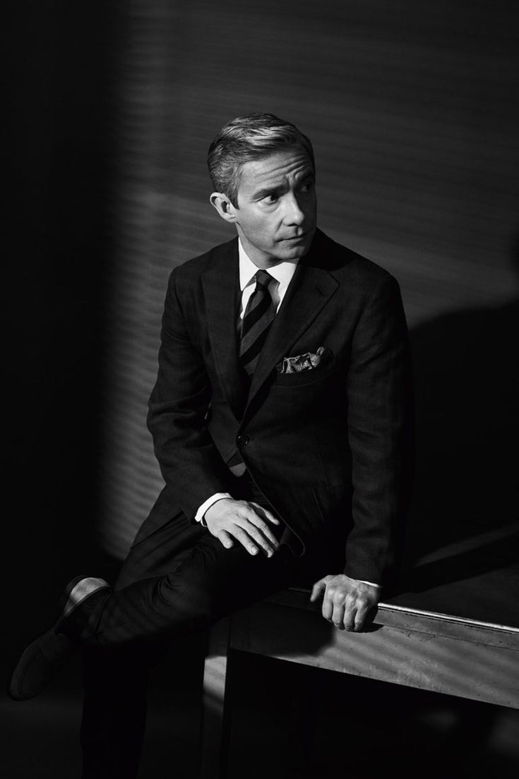 a man in a suit and tie sitting on a bench with his hand on his knee