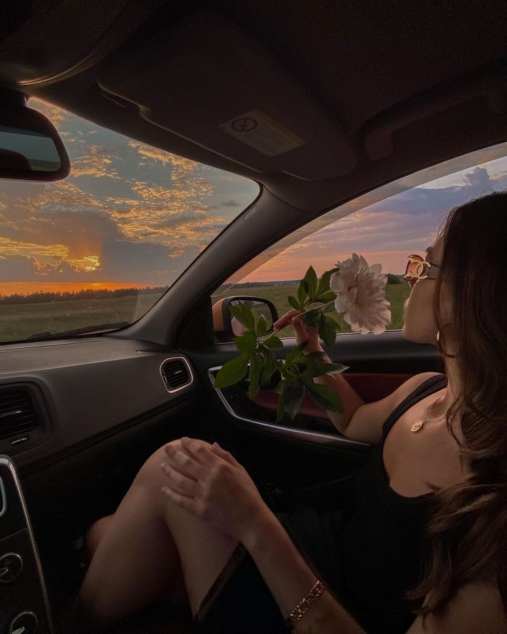 a woman sitting in the driver's seat of a car with flowers on the dashboard