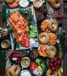 a table topped with bagels covered in salmon and cucumbers next to other foods