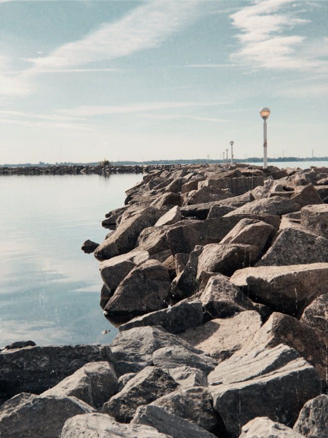 the rocks are lined up along the water's edge with a light pole in the distance