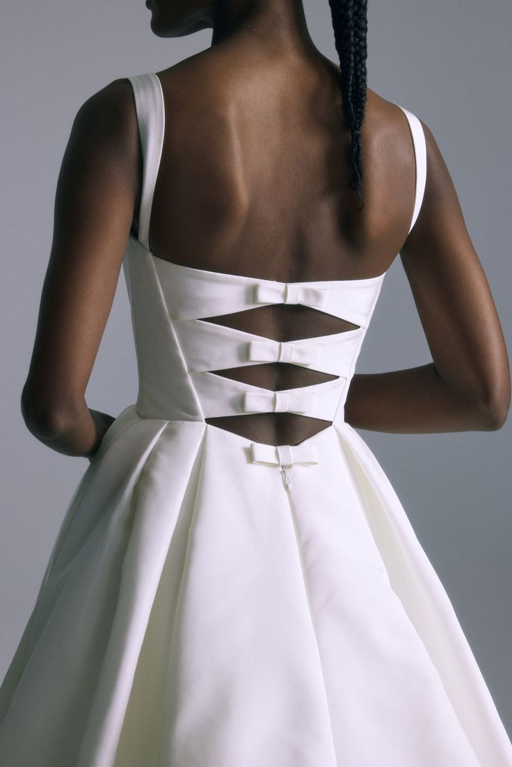 the back of a woman's white dress with cutouts on it and her hair in braids