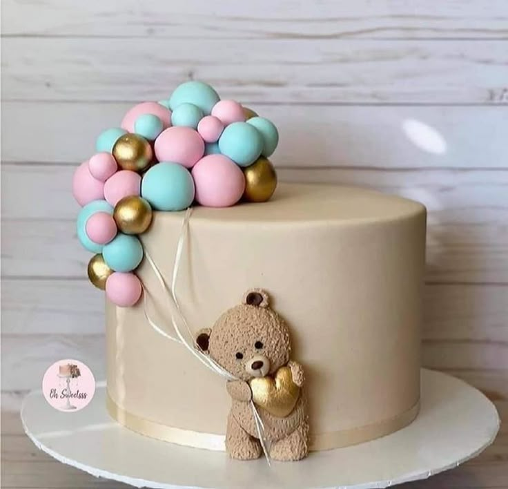 a teddy bear holding balloons on top of a cake