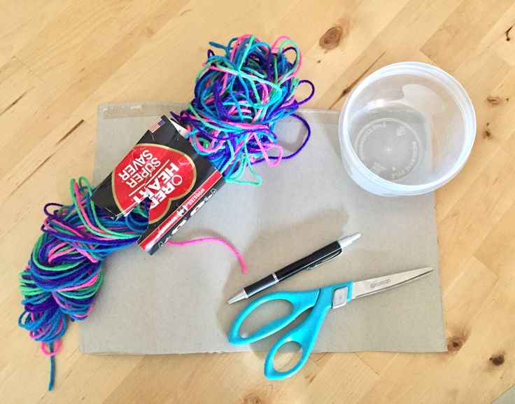 scissors, yarn and glue sitting on top of a piece of paper next to a cup