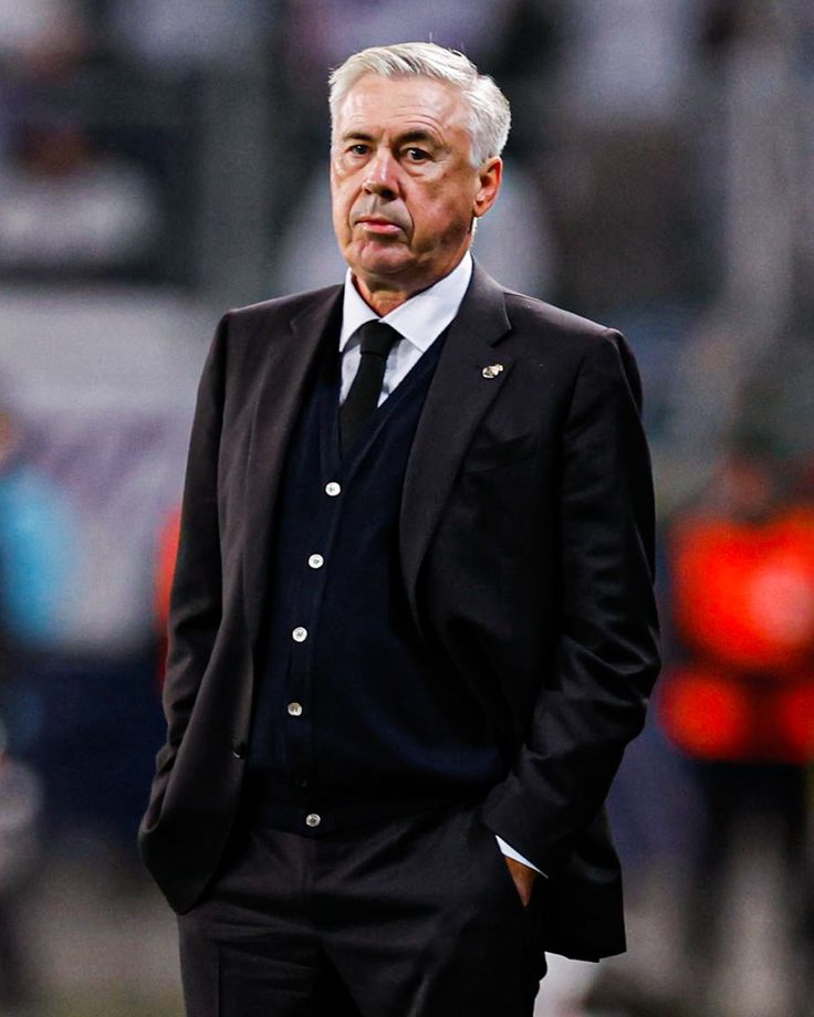 a man in a suit and tie standing on the sidelines at a soccer game