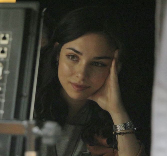 a woman sitting in front of a recording equipment with her hand on her head and looking at the camera