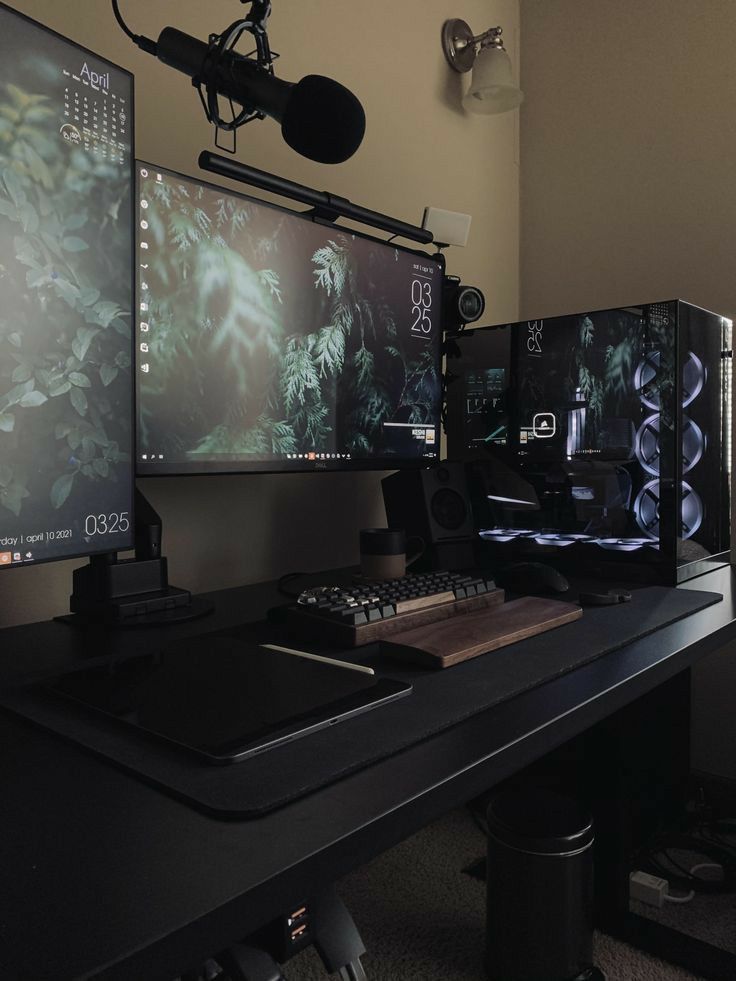 three computer monitors sitting on top of a desk next to a microphone and headphones