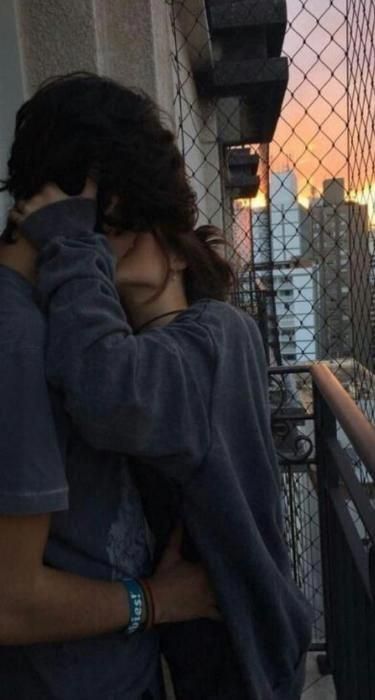 two people standing next to each other near a fence with the sun setting in the background