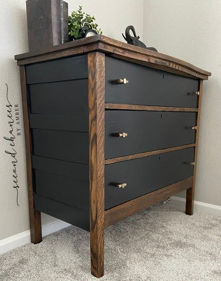 a black dresser with wooden drawers in a corner next to a white wall and carpeted floor