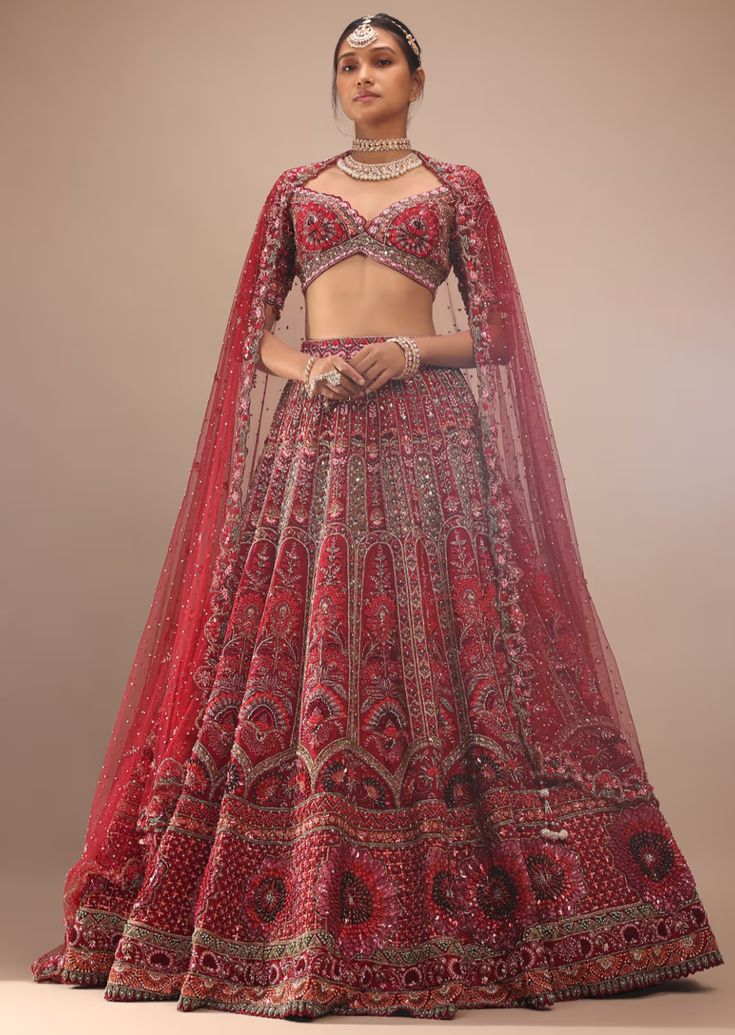 Dark red lehenga with a crop top in royal heritage embroidery.The lehenga comes in multi-color sequins, cut dana, stones, french knots 3D floral motifs embroidery, orange sequins, moti, and cut dana in half circle motifs, green cut dana, and stones in leaf shape motifs embroidery all over in kali design. The whole design is called embossed embroidery. The crop top comes in a plunging scalloped neckline with half sleeves and moti and beads fringes at the hemline. Red Embellished Sets For Navratri, Red Embellished Sharara For Navratri, Festive Red Lehenga With Mirror Work, Red Hand Embellished Saree Set, Red Hand Embellished Anarkali Set, Anarkali Style Red Hand Embellished Choli, Hand Embellished Red Lehenga For Reception, Bollywood Red Choli With Mirror Work, Bollywood Style Red Choli With Mirror Work