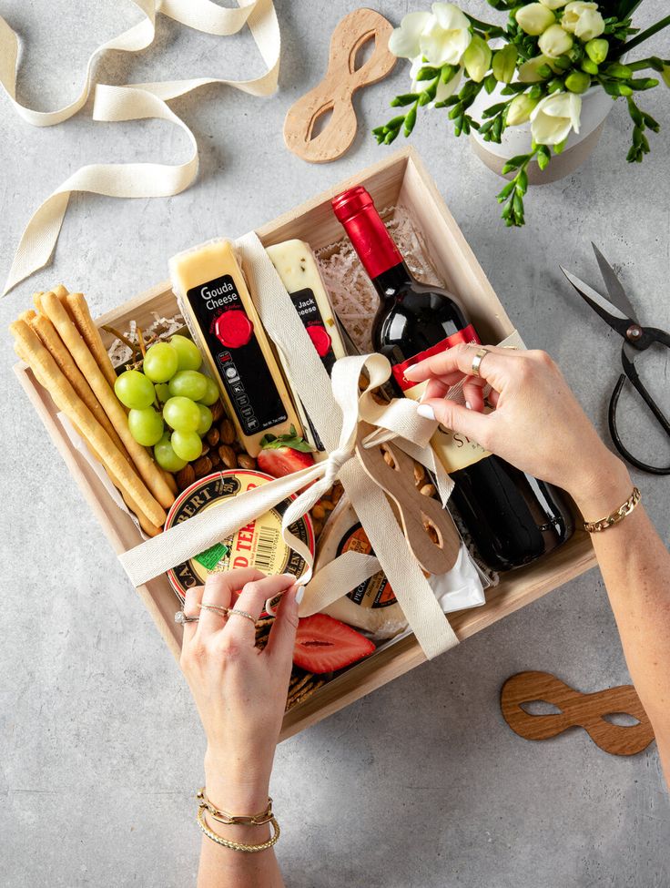 a woman is opening a wine box with cheese, grapes and crackers in it