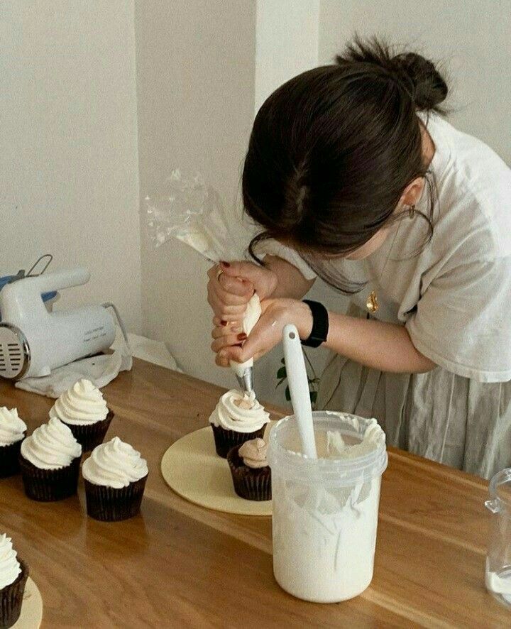 a woman is decorating cupcakes with icing on the table in front of her